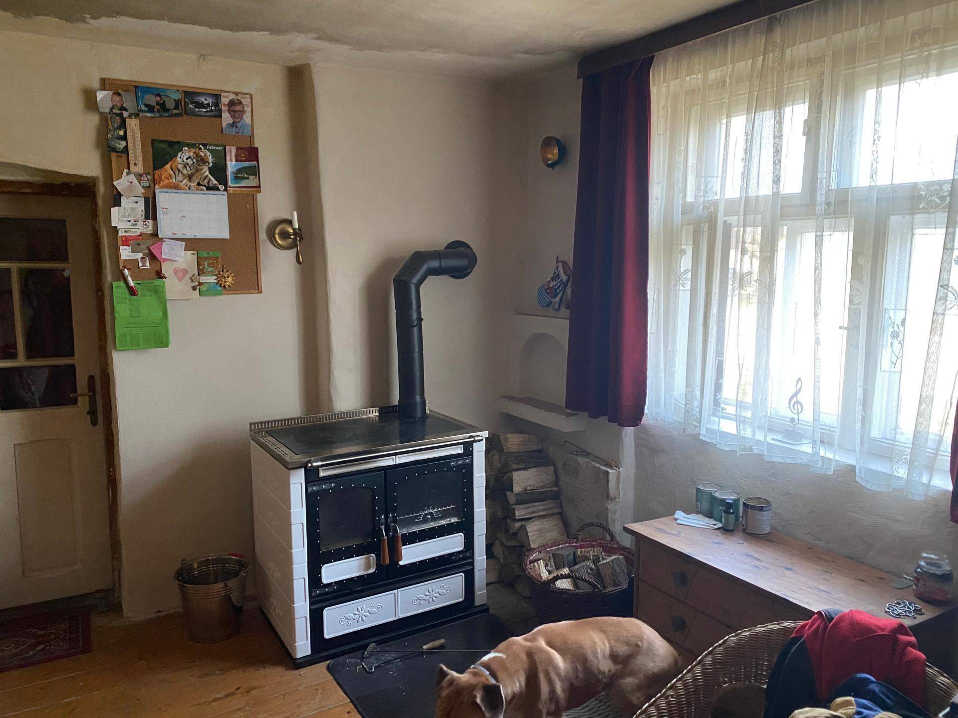 Raum mit traditionellem Kachelofen, Holzboden und großem Fenster für natürliches Licht.