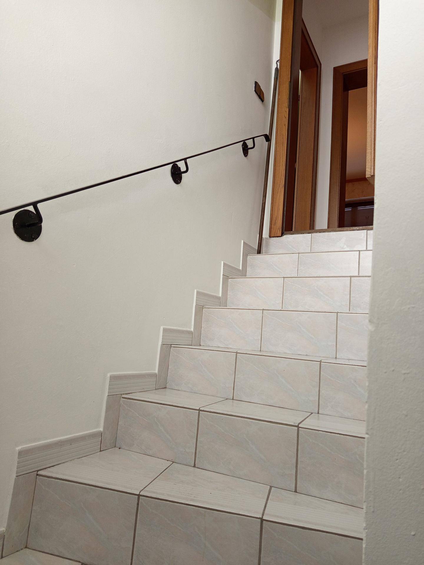 Innenliegende Treppe mit hellen Fliesen und einem schlichten schwarzen Handlauf.