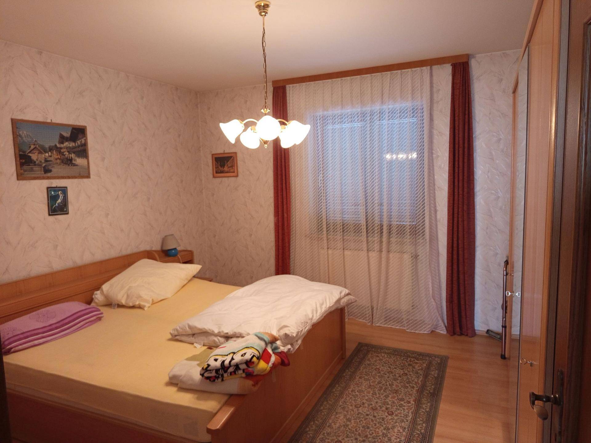 Schlafzimmer mit Doppelbett, Holzfußboden und gemusterter Tapete.