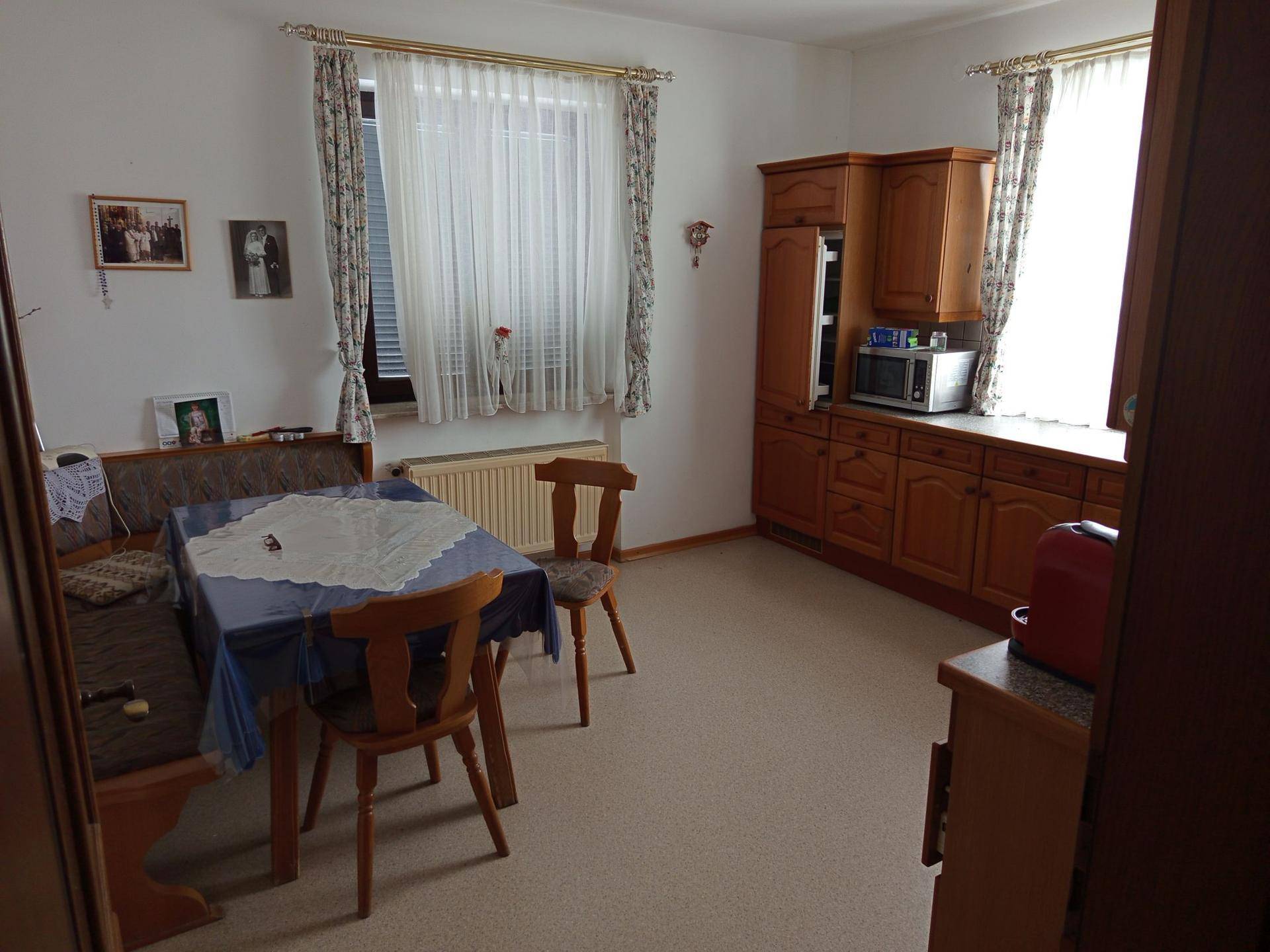 Gemütliche Wohnküche mit Holzeinbauten, Essbereich und Fenster mit Vorhängen.