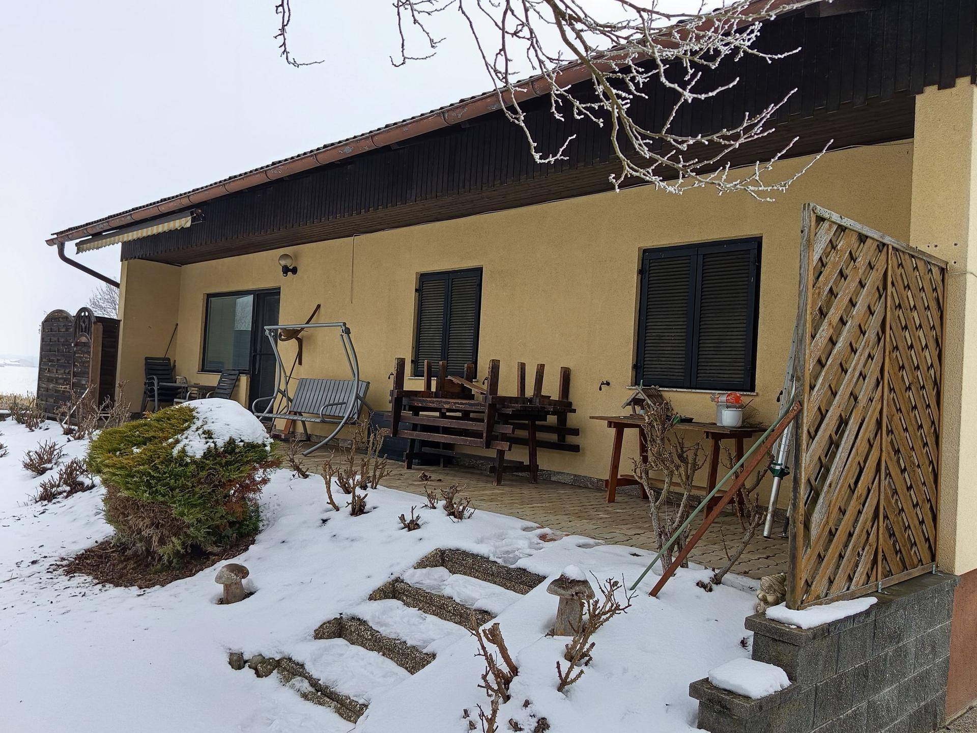 Hinterer Terrassenbereich des Hauses mit Sitzgelegenheiten und Schnee im Garten.