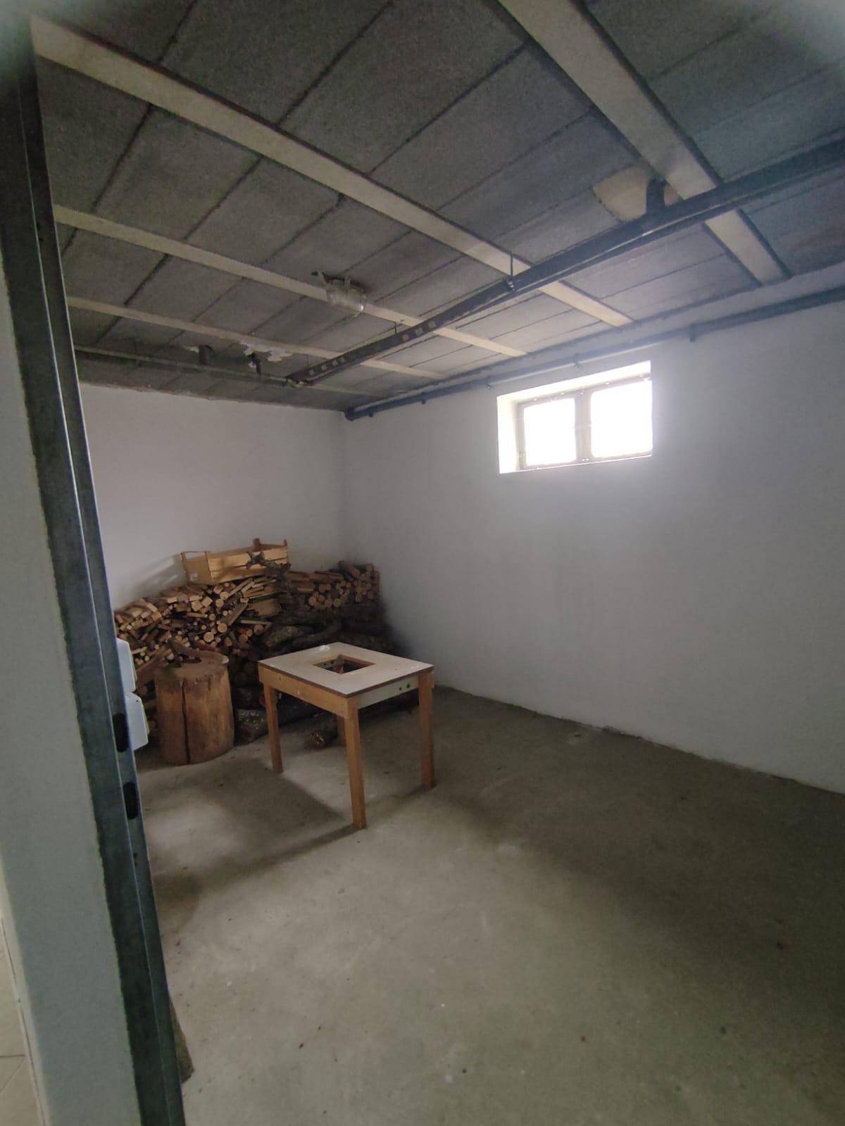 Kellerraum mit Betonboden und gestapeltem Brennholz, ideal als Lagerfläche.