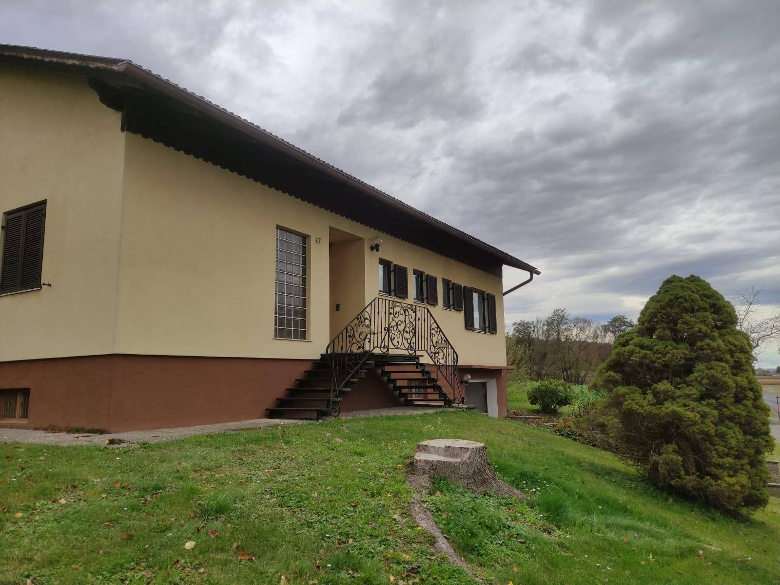 Seitenansicht des Hauses mit Garten und Blick auf die ländliche Umgebung unter bewölktem Himmel.