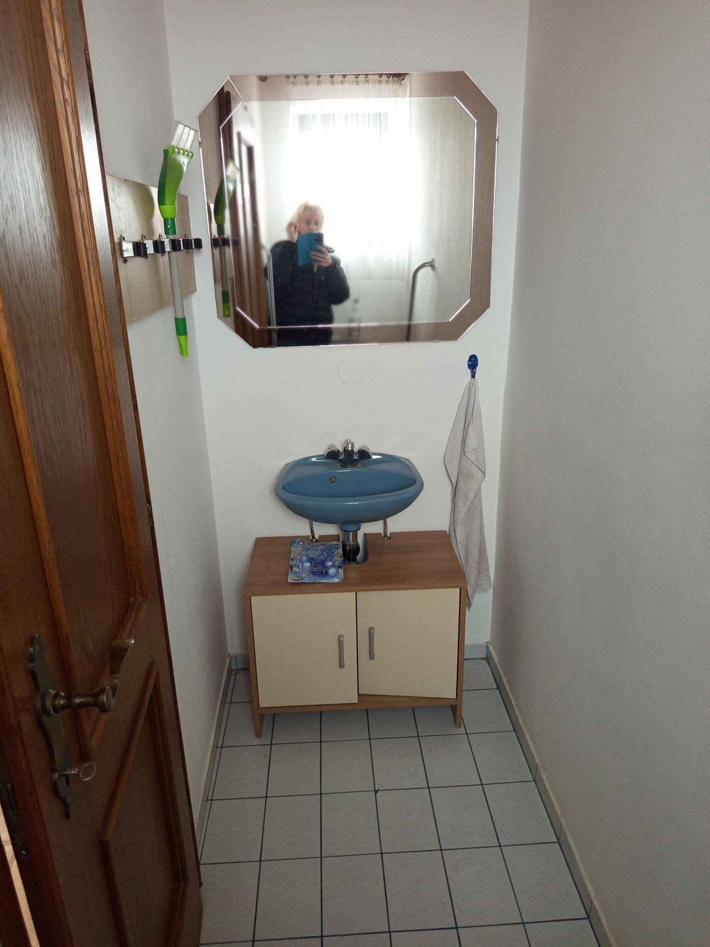 Kleine Gästetoilette mit Fliesenboden, Waschbecken und Spiegel.