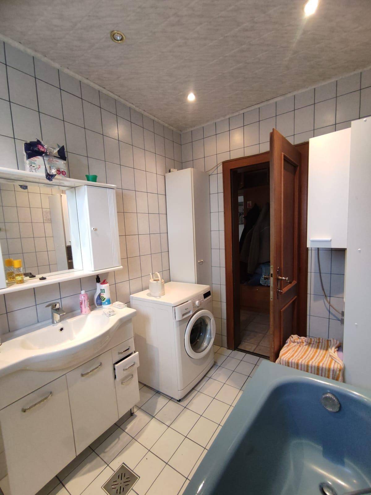 Badezimmer mit Fliesenboden, Badewanne, Waschmaschine und Spiegelschrank.