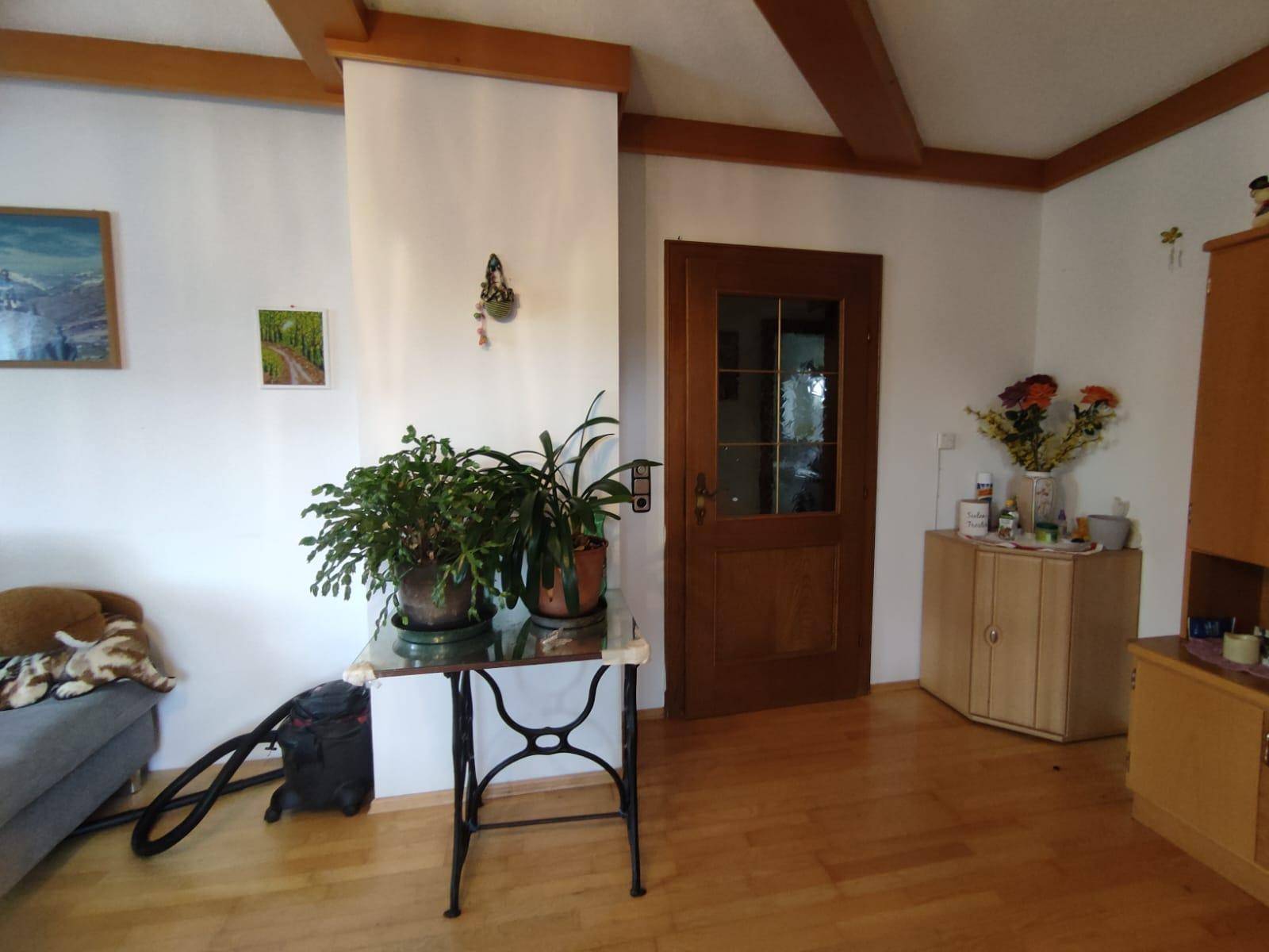 Wohnzimmer mit Holzbalkendecke, Parkettboden und Zugang zu weiteren Räumen.