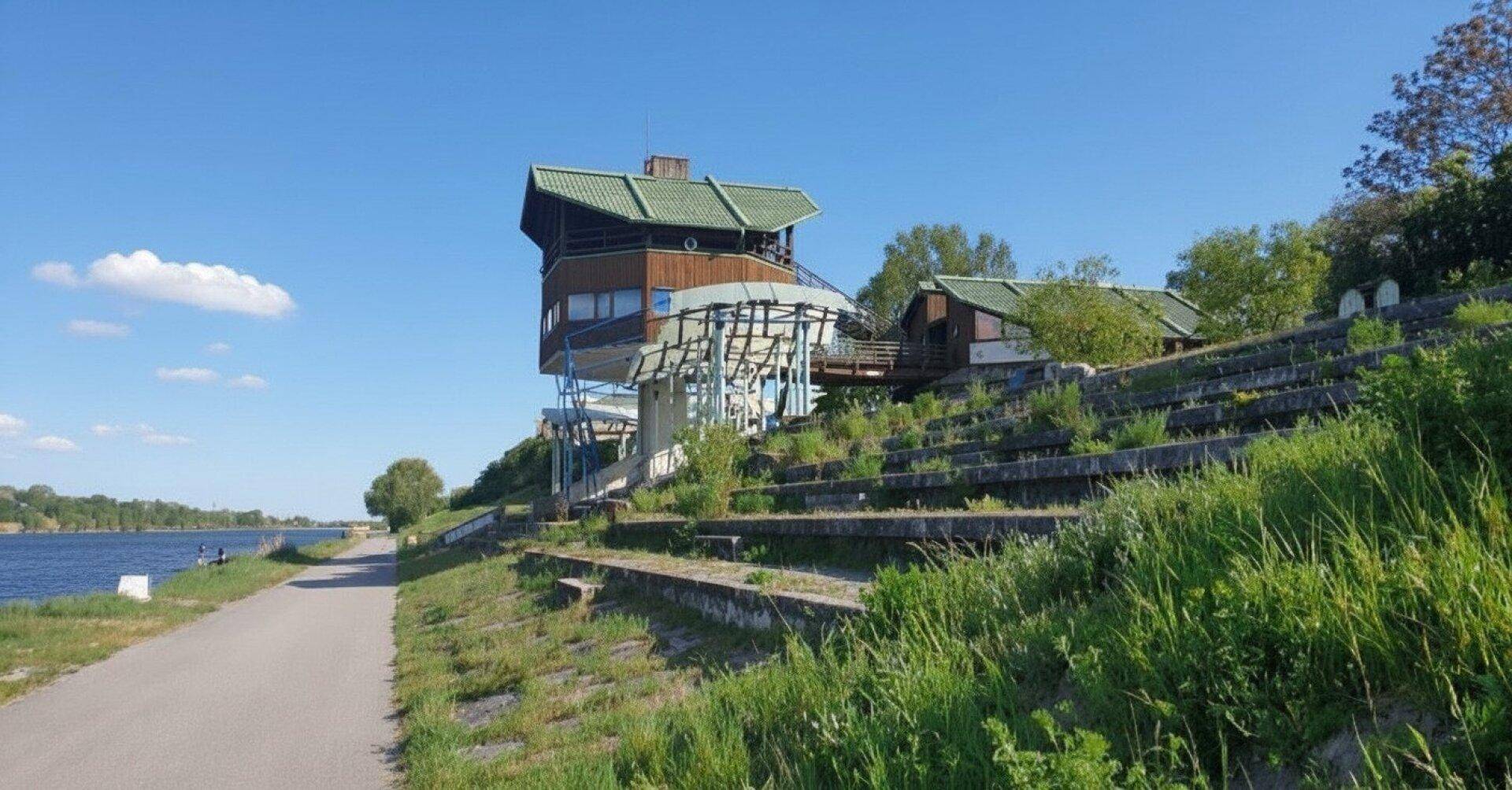 Architektonisch interessantes Gebäude am Ufer eines Gewässers mit Sitzstufen und Weg.