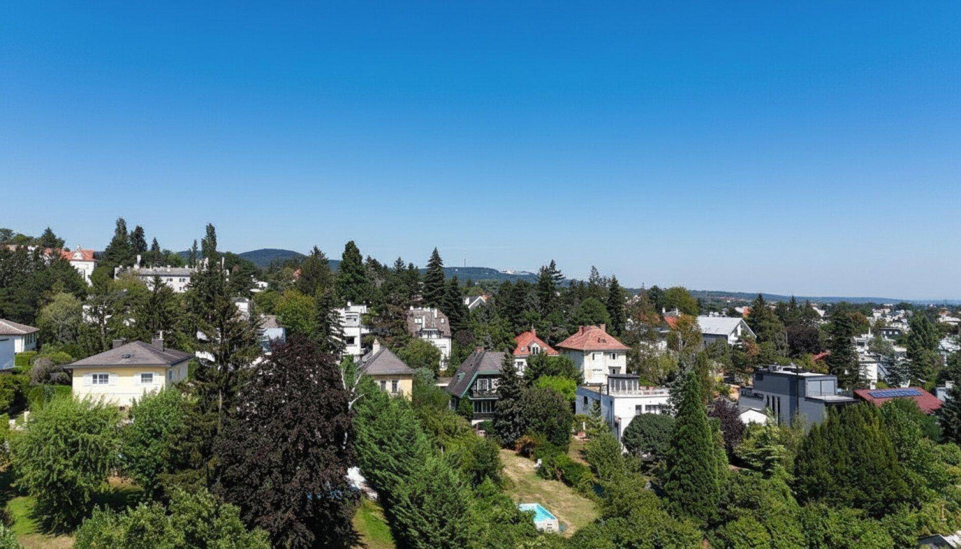 Panoramablick über eine grüne Wohnsiedlung mit vielen Bäumen und Häusern unter blauem Himmel.