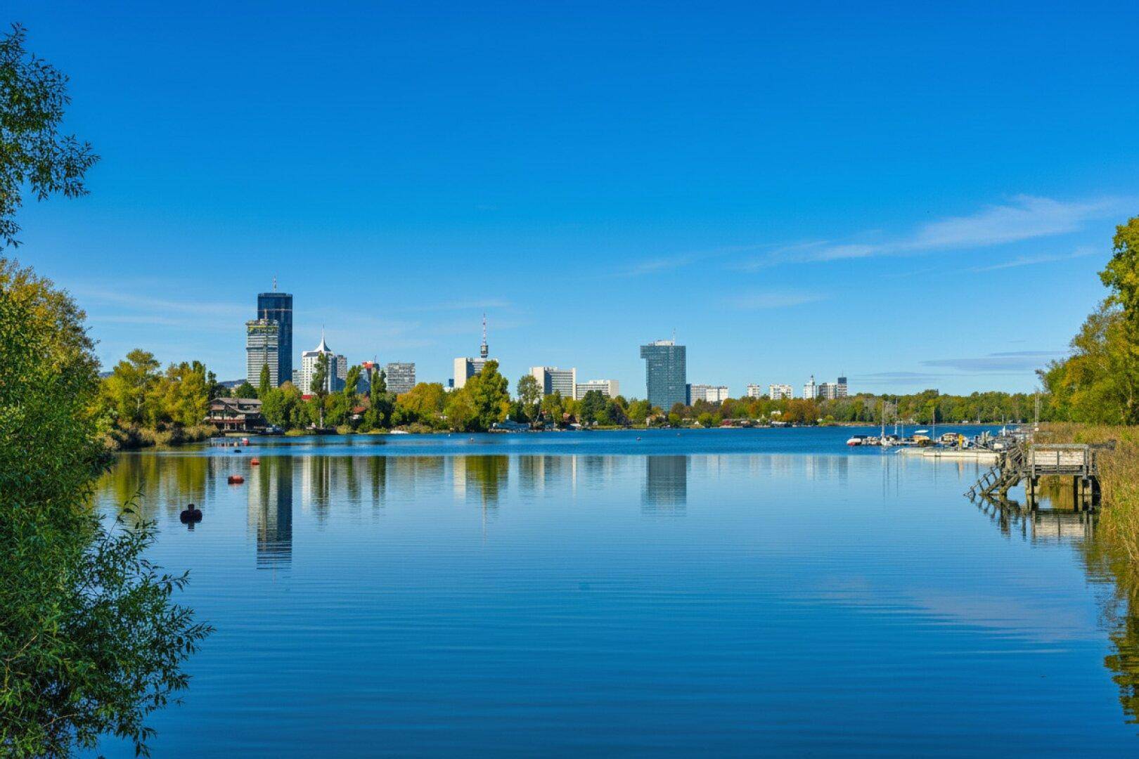 Malerischer See mit klarblauem Wasser und einer städtischen Skyline im Hintergrund.