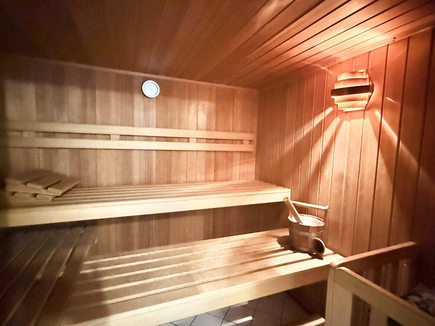 Holzvertäfelte Sauna mit Bänken, Eimer und Kelle für entspannende Wellnessmomente.