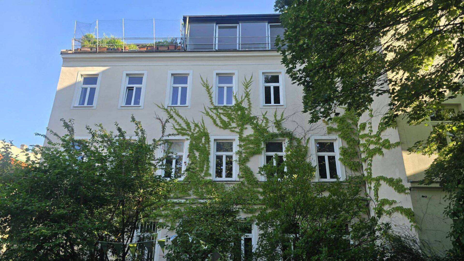 Gebäudefassade mit Efeubewuchs und einem Dachgeschossausbau mit sichtbarer Dachterrasse.