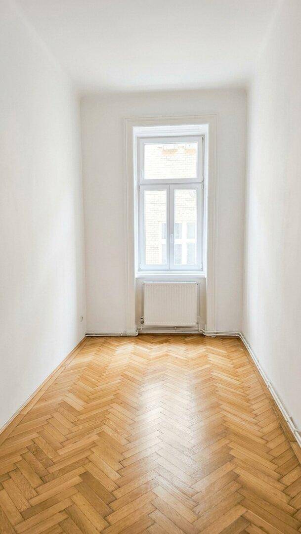 Kleiner, heller Raum mit Fischgrätparkett und einem Fenster, ideal als Schlaf- oder Arbeitszimmer.