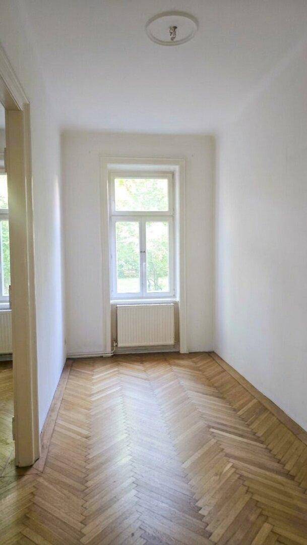 Langer Flur mit klassischem Fischgrätparkett und einem Fenster, das den Raum erhellt.