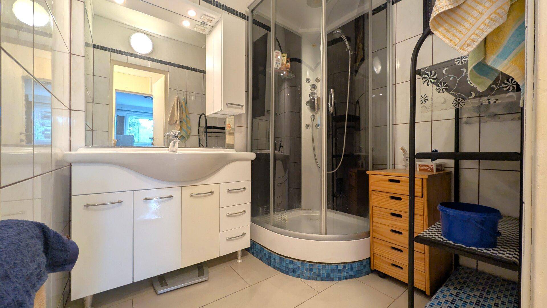Funktionales Badezimmer mit Duschkabine, Waschbeckenunterschrank und hellen Fliesen.