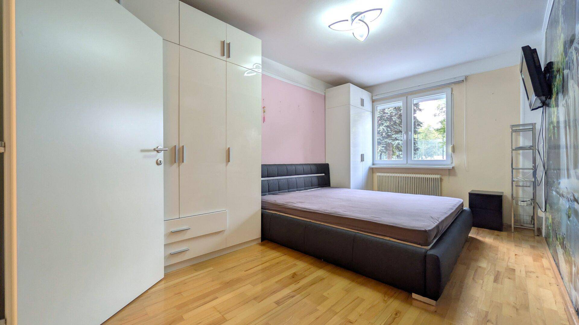 Gemütliches Schlafzimmer mit Holzboden, großem Kleiderschrank und Fenster mit Blick ins Grüne.