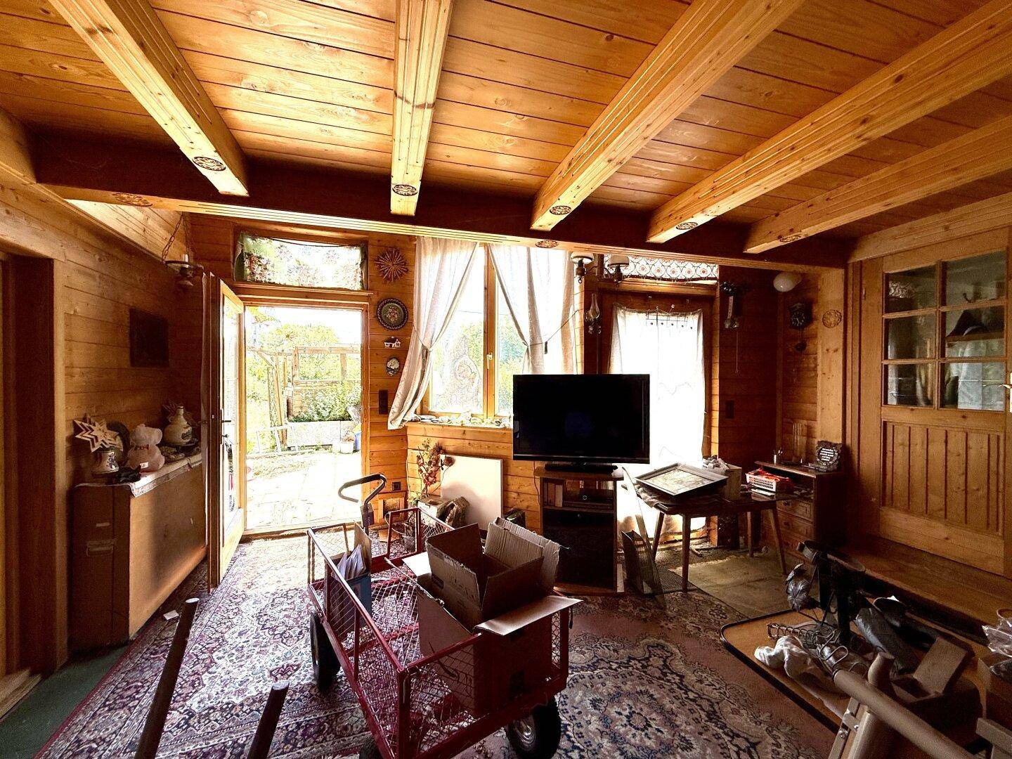Gemütlicher Wohnbereich mit viel Holz, Fernseher und Zugang zum sonnigen Außenbereich.