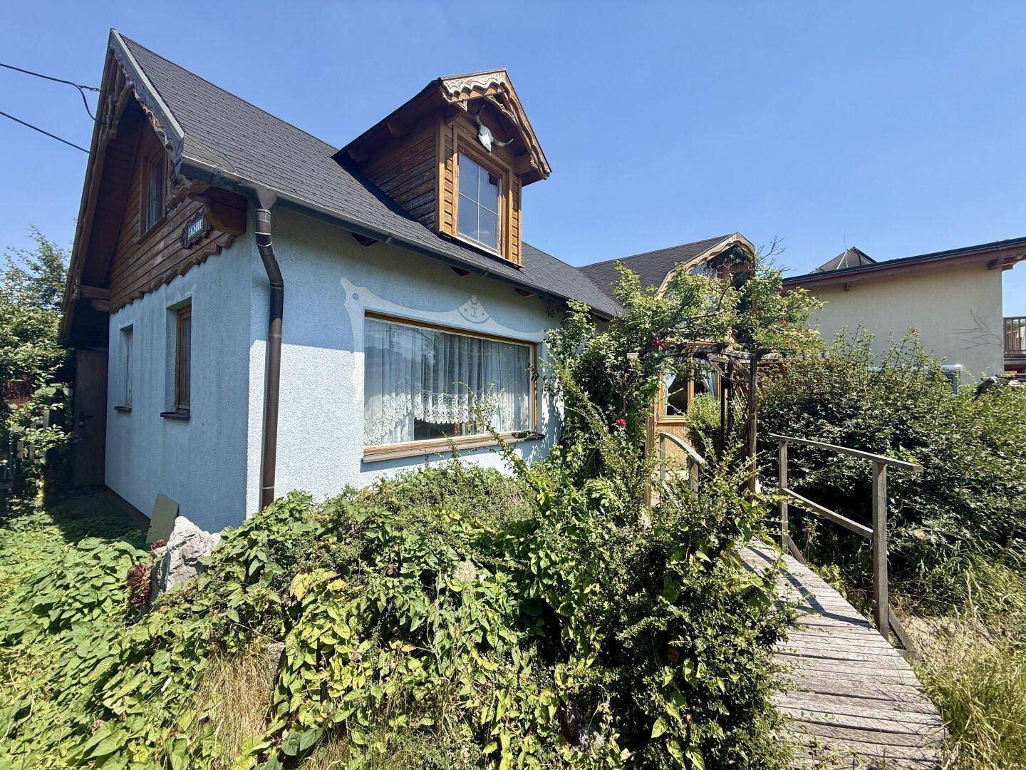 Seitenansicht des Hauses mit hellblauer Fassade, Holzelementen und einem kleinen Steg.