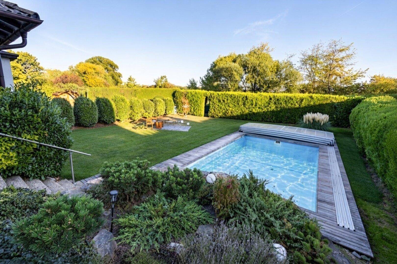 Gepflegter Garten mit Swimmingpool, umgeben von hohen Hecken und üppiger Vegetation.