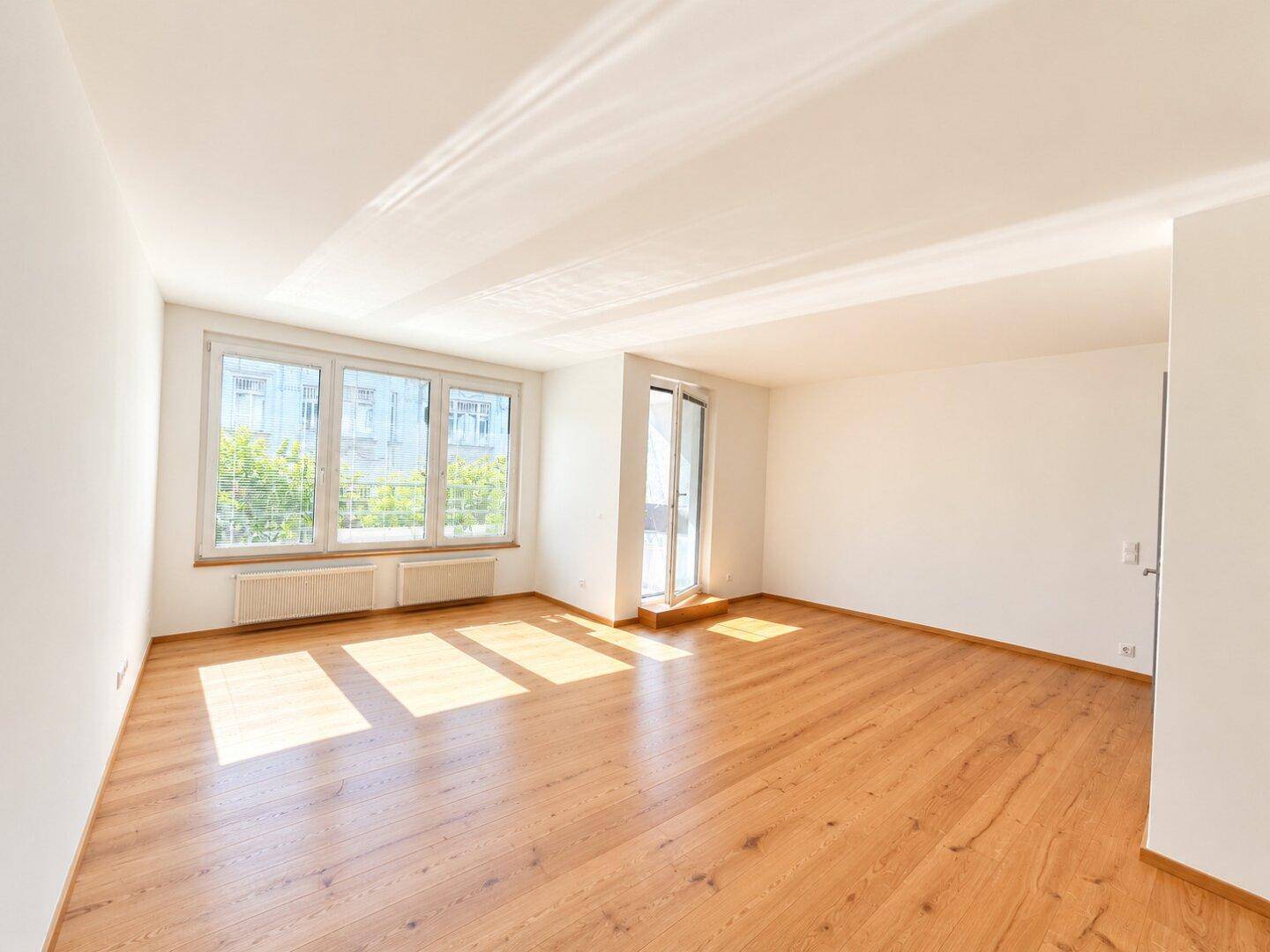 Lichtdurchflutetes Wohnzimmer mit Eichenparkett und großen Fenstern, die viel Sonne hereinlassen.
