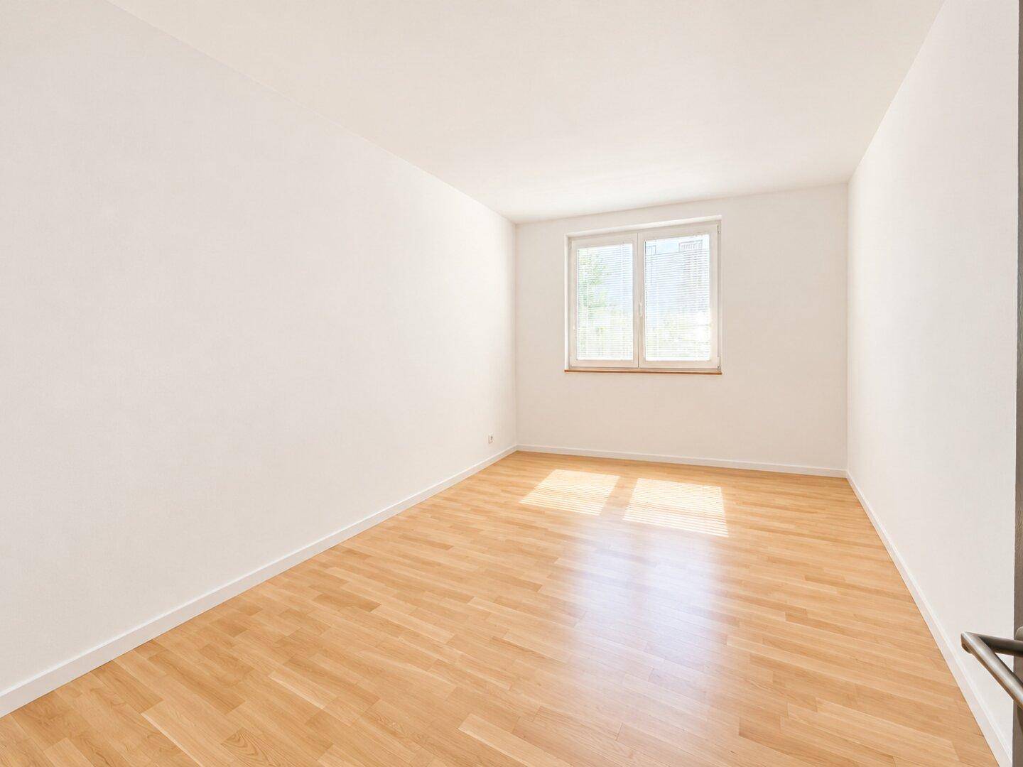 Helles Schlafzimmer mit Holzboden und einem Fenster, das viel Tageslicht spendet.