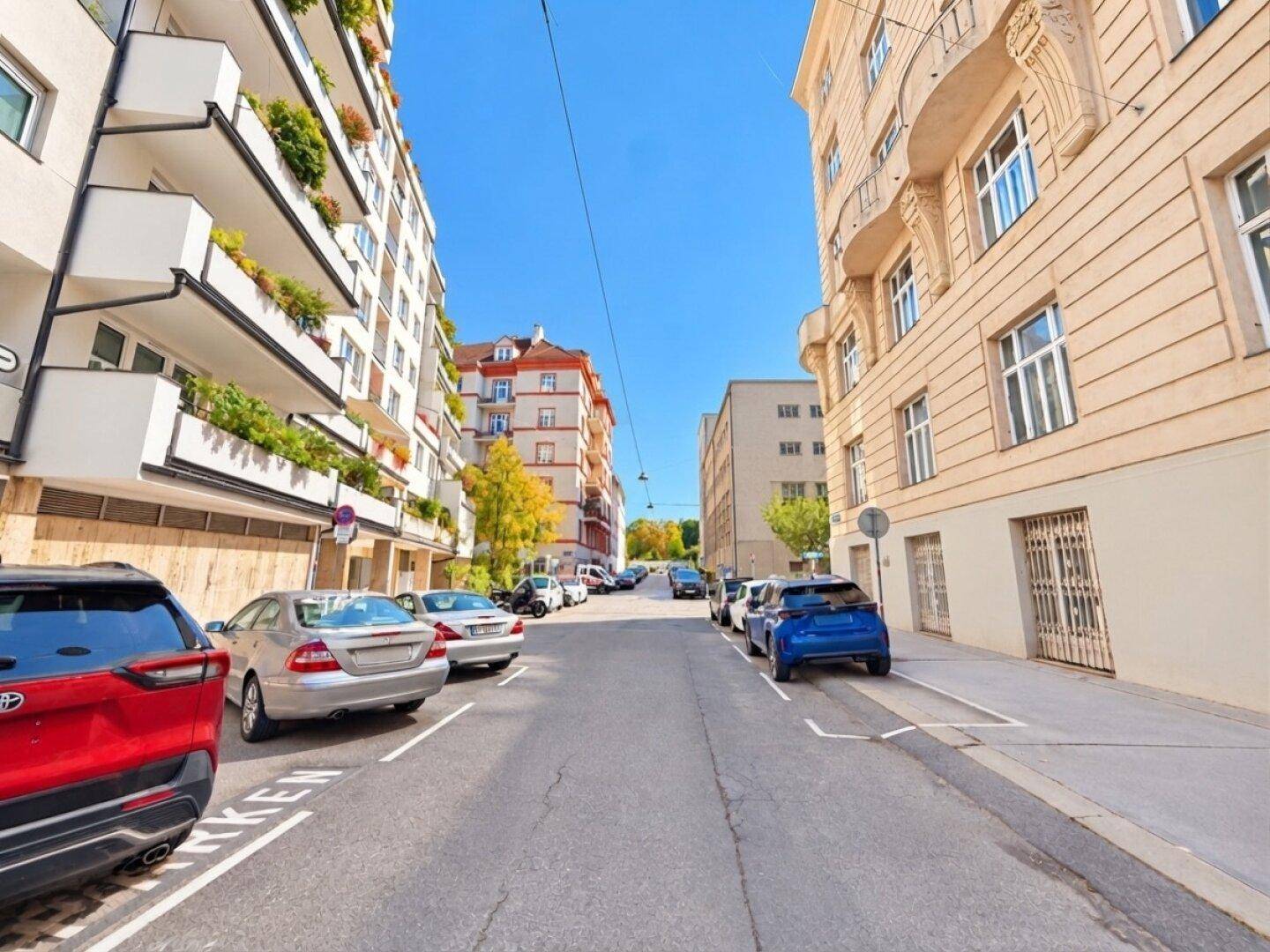 Ruhige Wohnstraße mit parkenden Autos und historischen Gebäuden unter blauem Himmel.