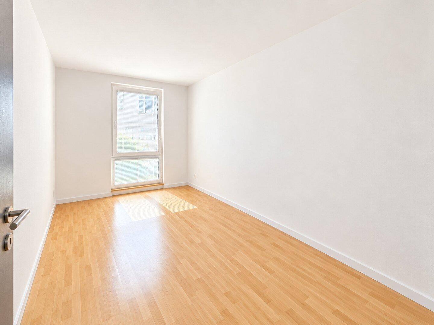 Geräumiges Schlafzimmer mit Parkettboden und einem großen Fenster für natürliche Belichtung.