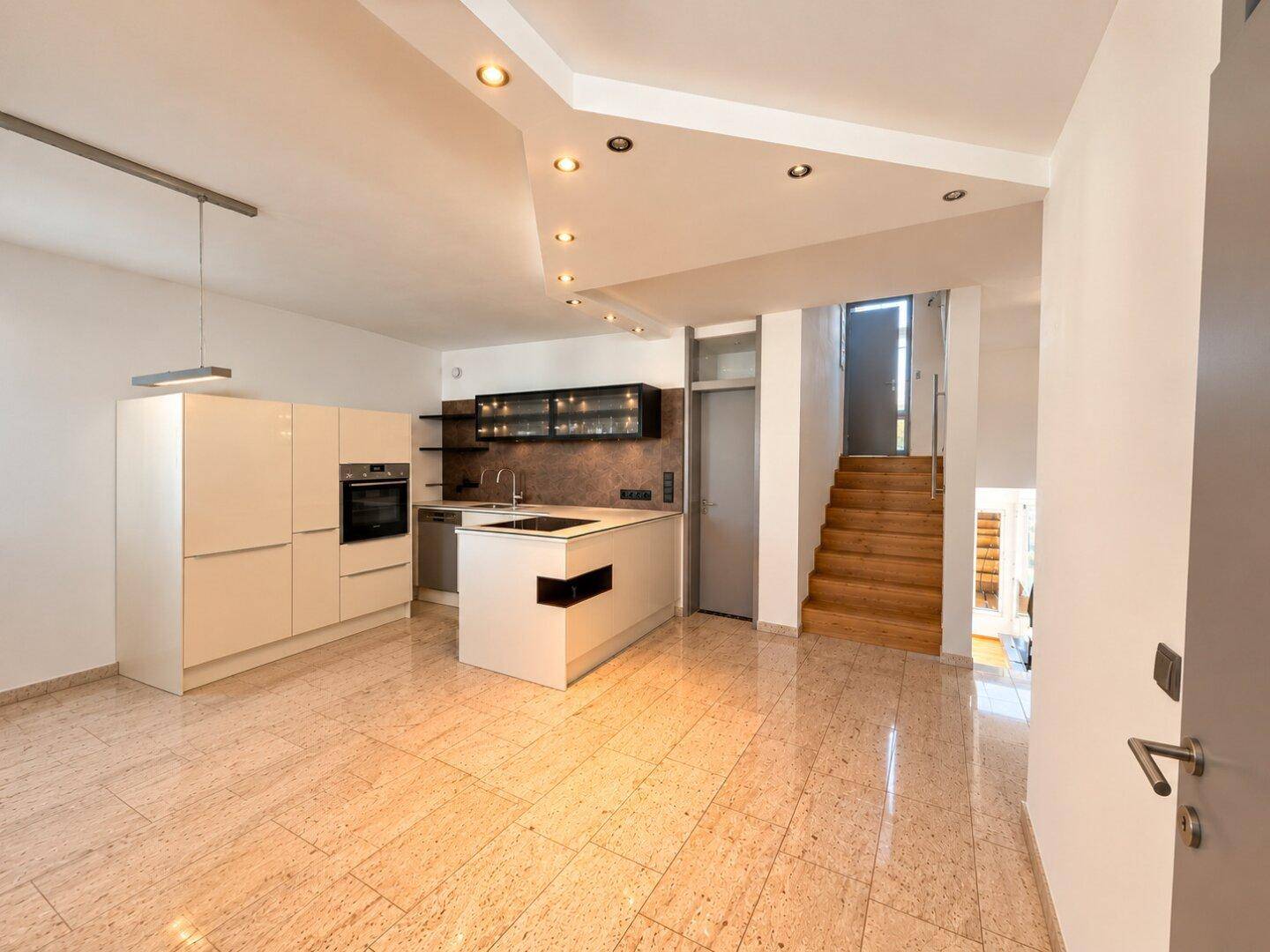 Moderne offene Küche mit Kochinsel und Fliesenboden, angrenzend an den Wohnbereich mit Treppe.