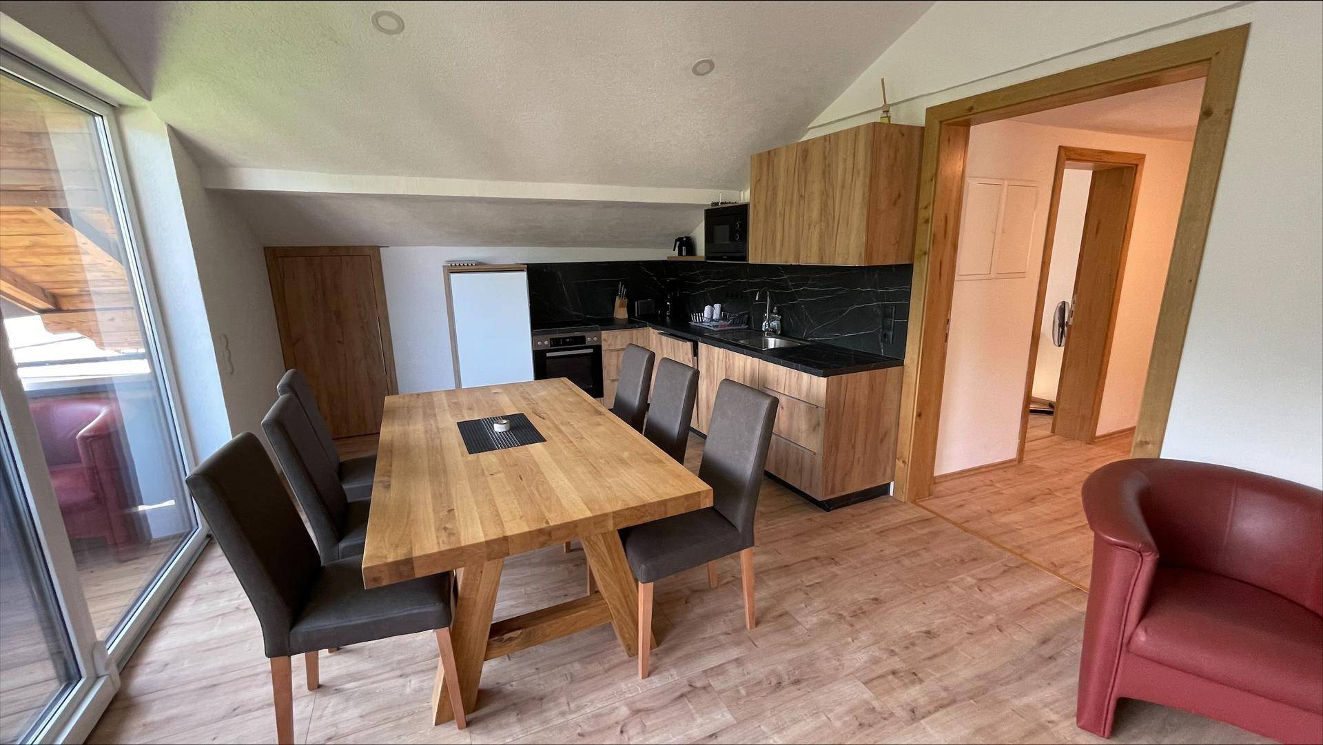 Moderne Küche mit Essbereich im Dachgeschoss, Holzelementen und Zugang zum Balkon.