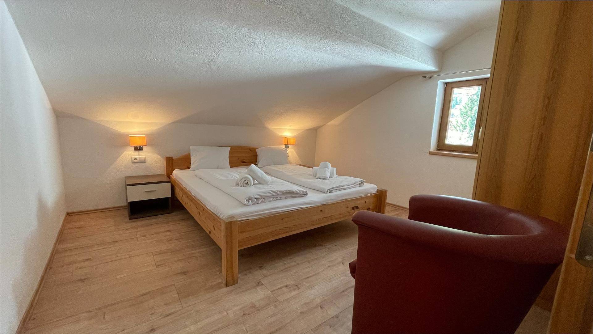 Helles Schlafzimmer im Dachgeschoss mit Doppelbett, Holzboden und rotem Sessel.