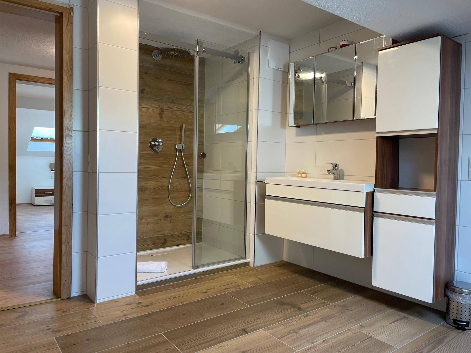 Modernes Badezimmer mit Duschkabine, schwebendem Waschtisch und Holzelementen.