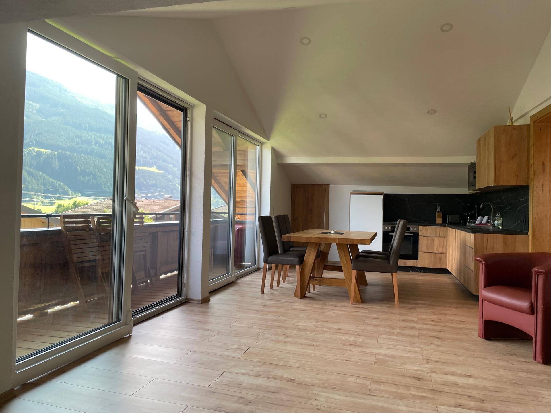 Offener Wohnbereich mit Küche und Essbereich im Dachgeschoss, großen Fenstern und Bergblick.