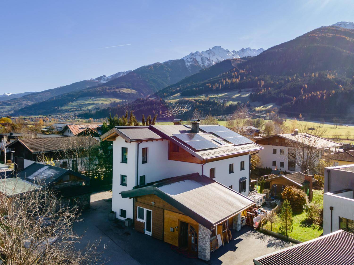 Luftaufnahme eines modernen Hauses mit Solaranlage auf dem Dach und beeindruckendem Bergpanorama.