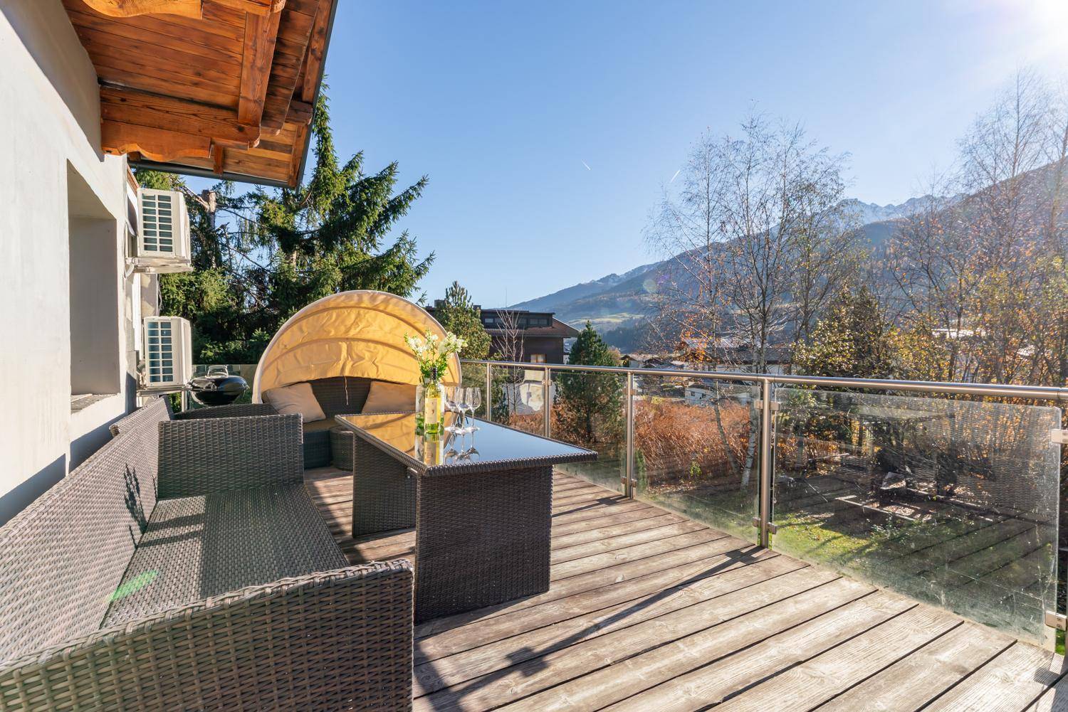 Sonniger Balkon mit Rattanmöbeln, Glasgeländer und weitem Blick auf die Berge und das Tal.