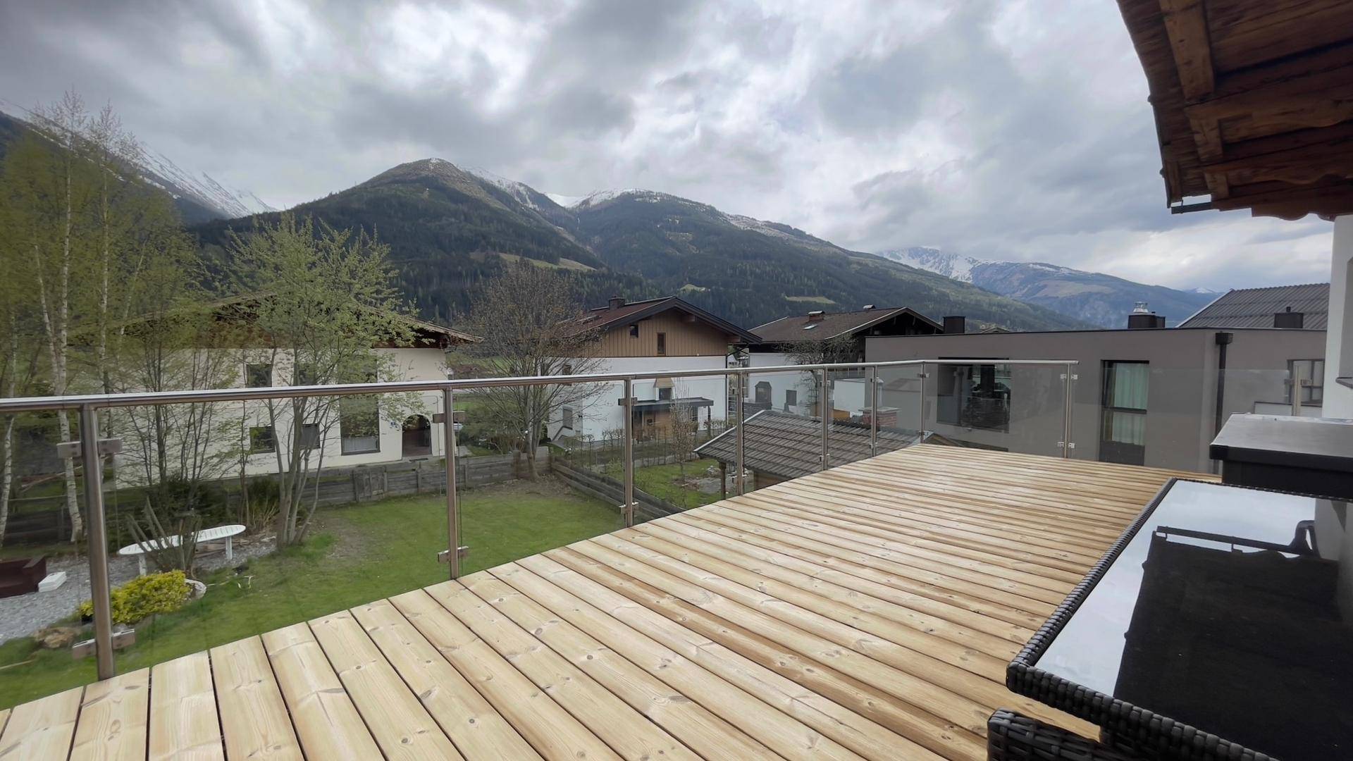 Große Holzterrasse mit Glasgeländer und weitem Blick auf die Berge und die Umgebung.