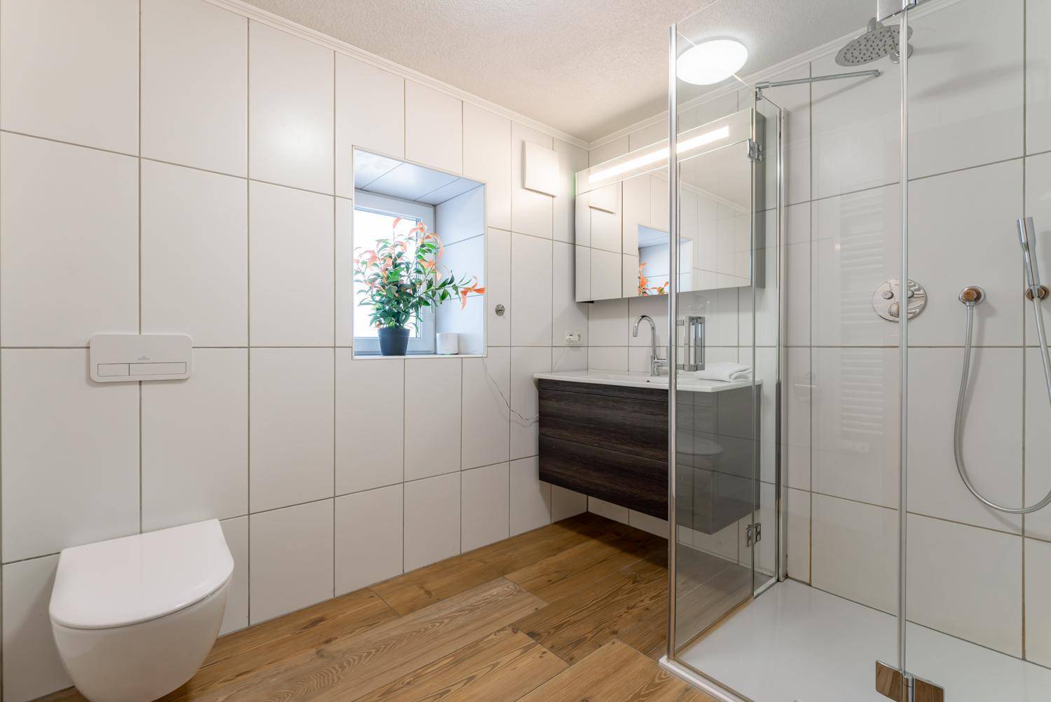 Modernes Badezimmer mit Duschkabine, wandhängendem WC und Holzbodenoptik.