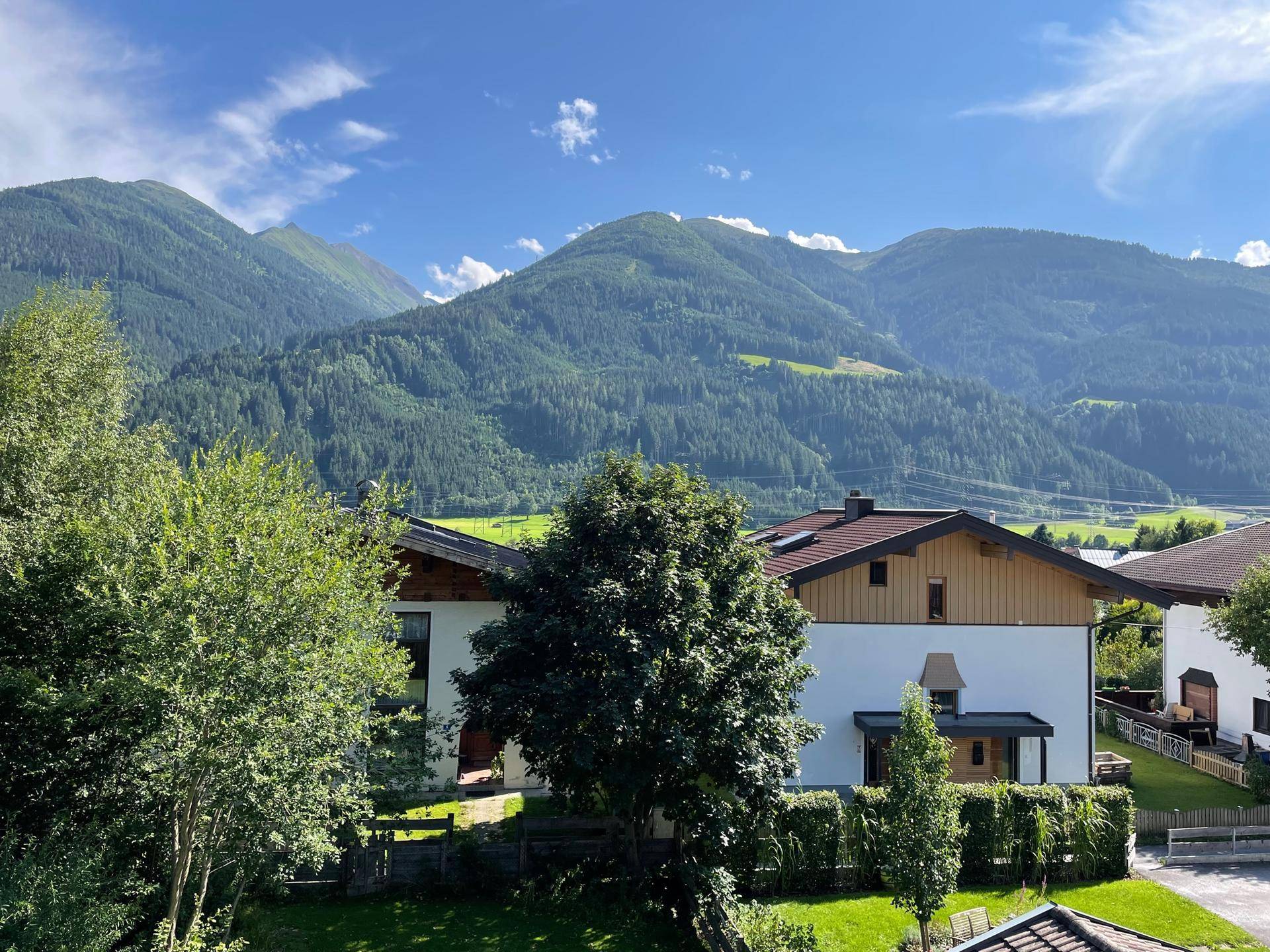 Malerische Berglandschaft mit grünen Bäumen und Häusern unter blauem Himmel.