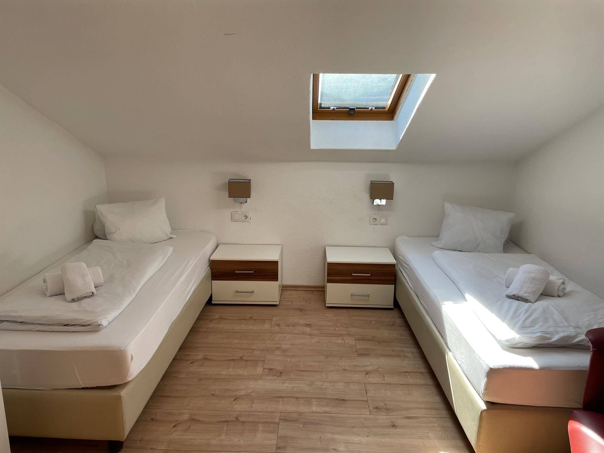 Helles Schlafzimmer im Dachgeschoss mit zwei Einzelbetten, Dachfenster und Holzboden.