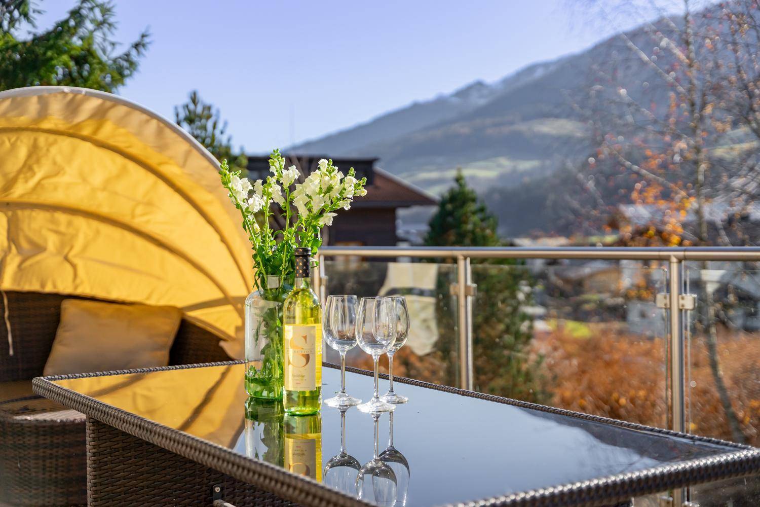 Detailaufnahme des Balkons mit Getränken und Blumen, umgeben von einer malerischen Berglandschaft.