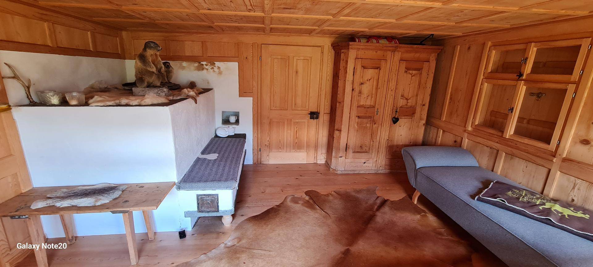 Rustikales Wohnzimmer mit Holztäfelung, Kachelofen und traditionellen Einrichtungsgegenständen.