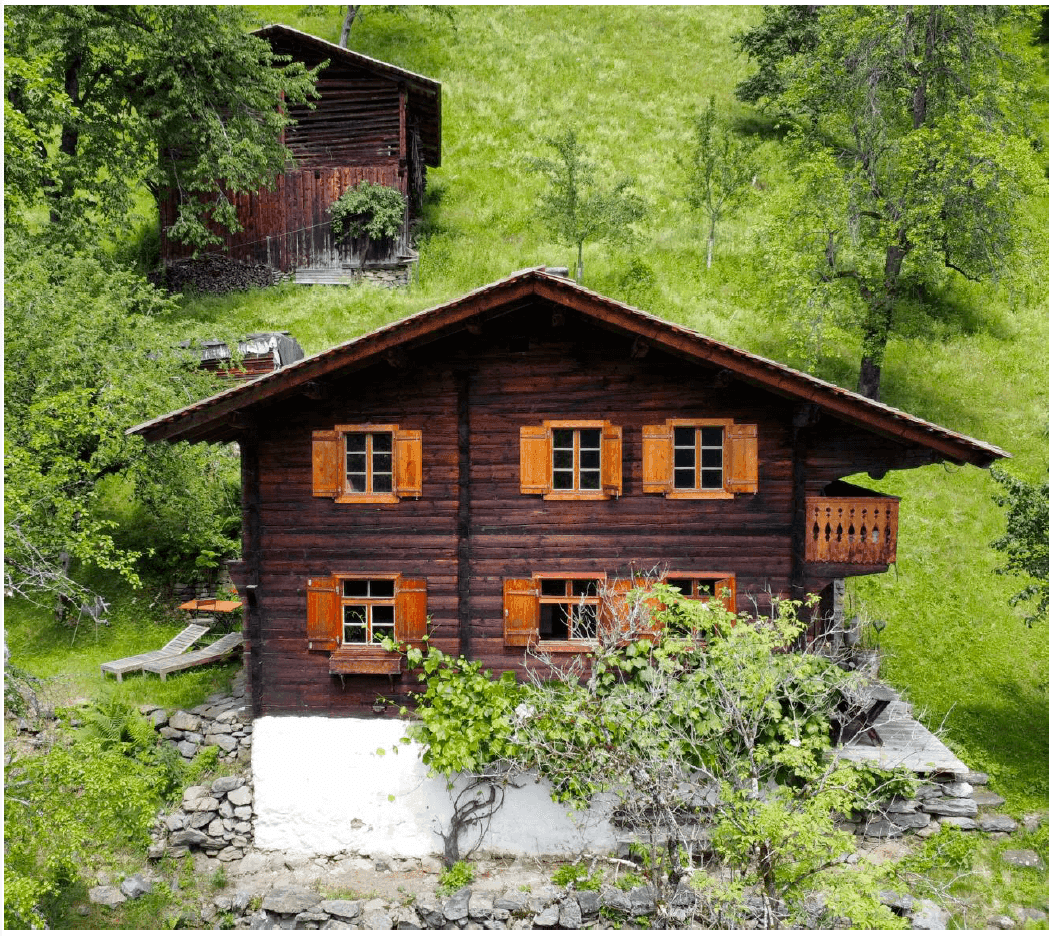 Traditionelles Holzhaus mit Holzbalkon und grüner Umgebung in den Bergen.