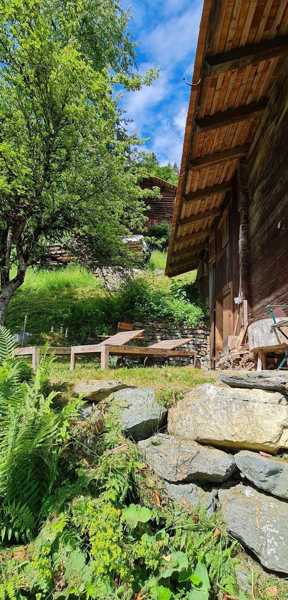 Rustikales Holzhaus mit einer kleinen Terrasse und Liegestühlen im Gartenbereich.