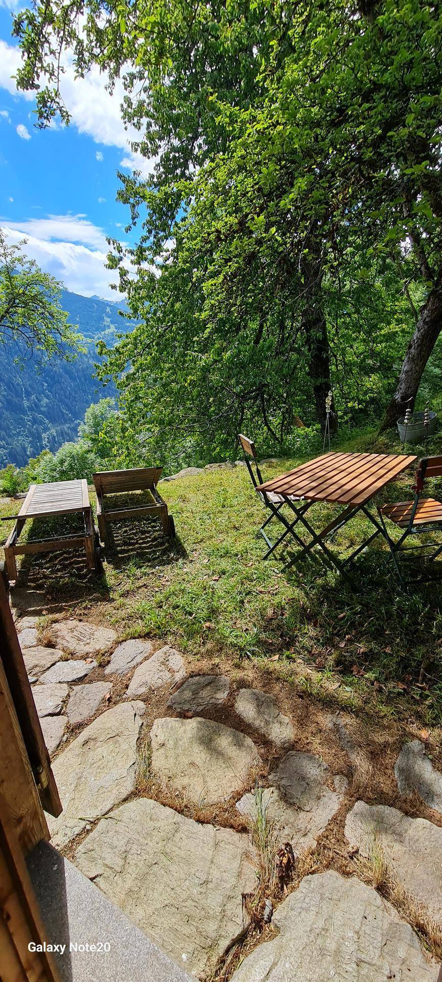 Gemütlicher Sitzbereich im Freien mit Holztisch und Stühlen, umgeben von Natur und Bergblick.
