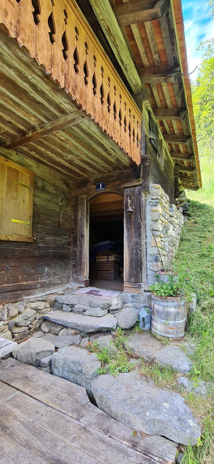 Traditioneller Hauseingang aus Holz und Stein mit einem darüberliegenden geschnitzten Holzbalkon.