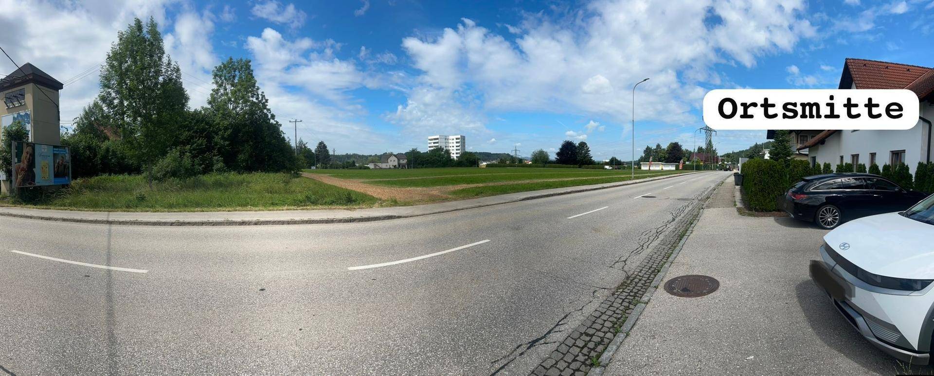 Panoramablick auf die Ortsmitte mit Straße, unbebautem Grundstück und geparkten Autos.