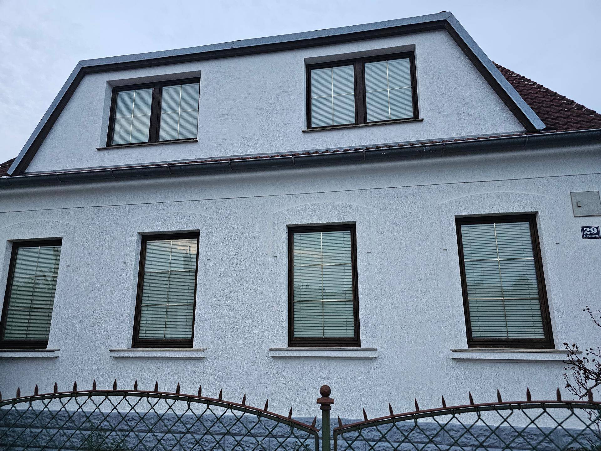 Nahaufnahme der weißen Fassade mit braunen Fenstern und Dachgauben des Einfamilienhauses.