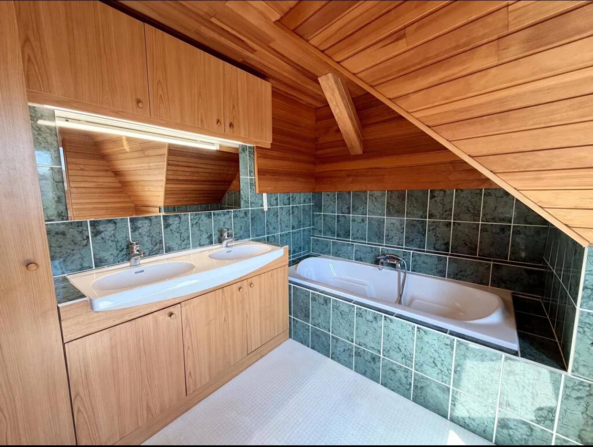 Badezimmer im Dachgeschoss mit Doppelwaschbecken, Badewanne und Holzverkleidung an Wänden und Decke.