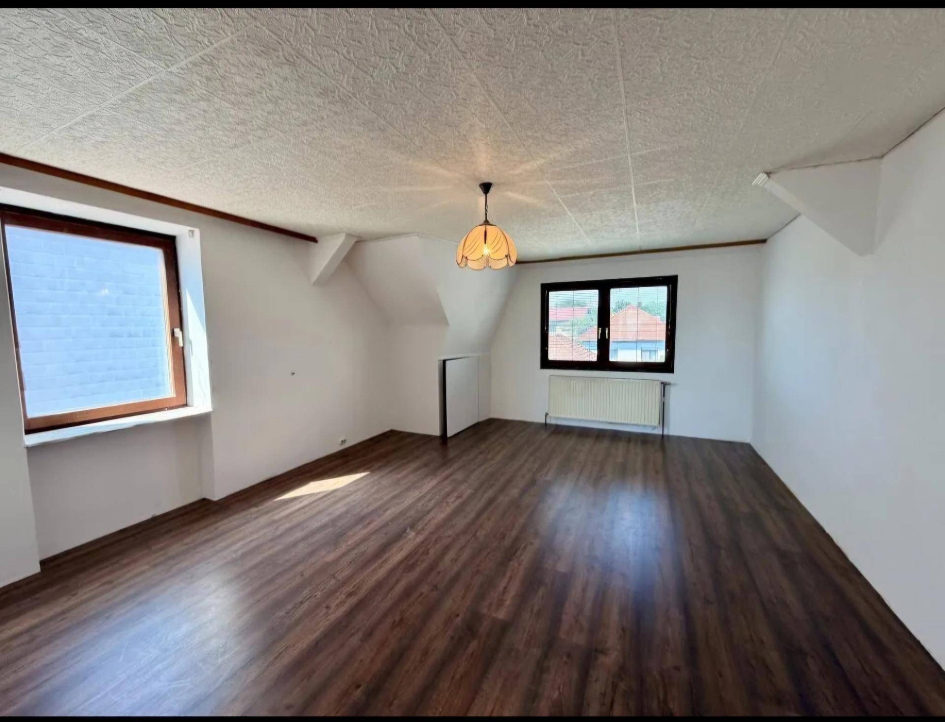 Helles Zimmer im Dachgeschoss mit Laminatboden, schrägen Wänden und Fenster.
