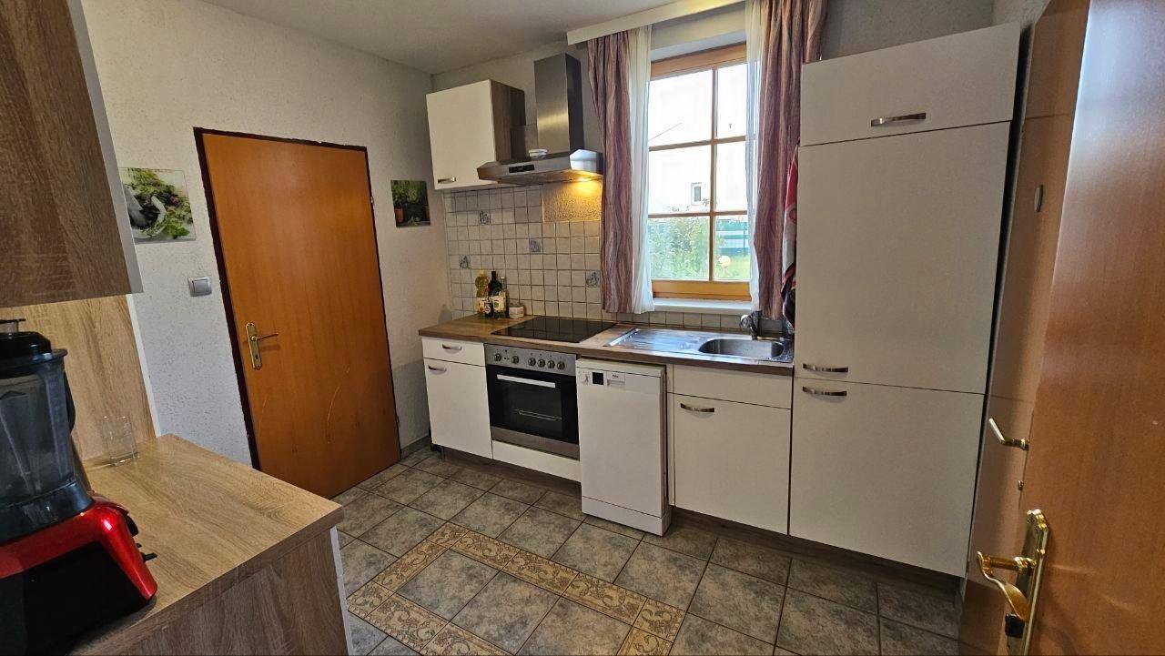 Funktionale Küche mit weißen Schränken, Fliesenboden, Spülmaschine und einem Fenster.