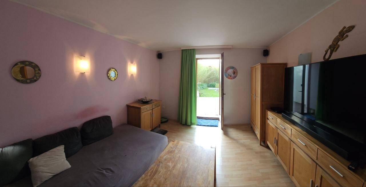 Wohnzimmer mit Sofa, Holzmöbeln und einem Ausgang zum Garten, gut beleuchtet.