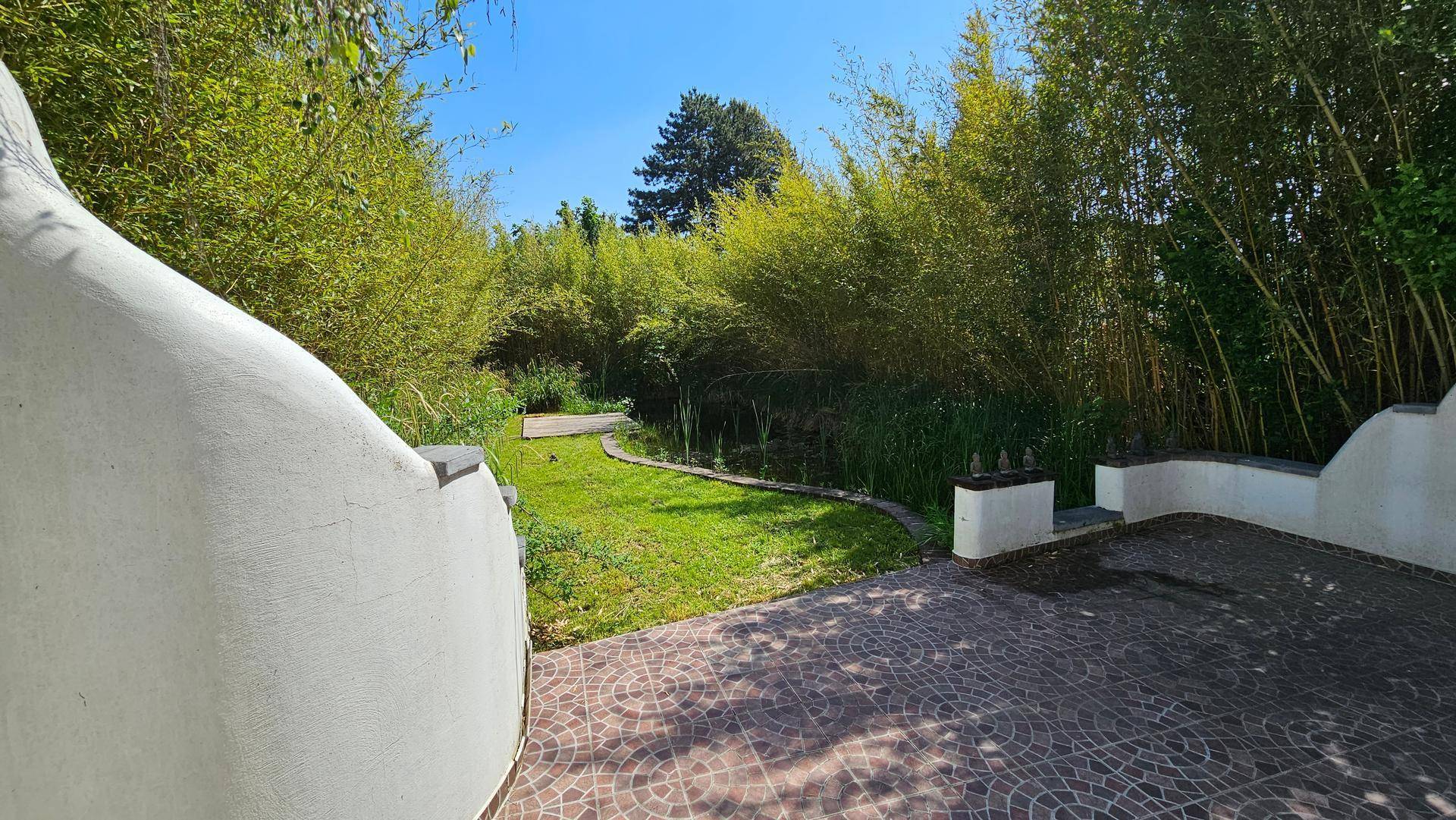 Gepflasterte Terrasse mit dekorativen Fliesen, die zu einem grünen Garten mit Teich und Bambus führt.